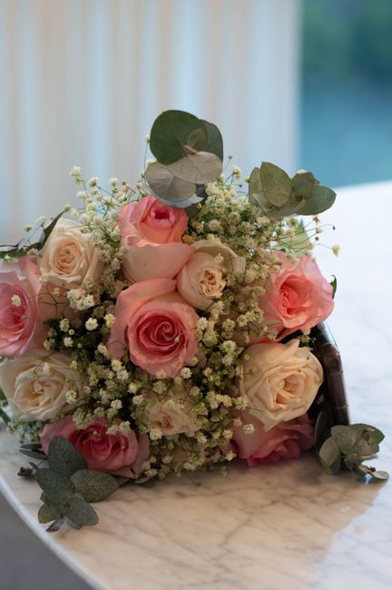 A floral bouquet featuring a combination of pale pink and cream roses, arranged with sprigs of white baby's breath and eucalyptus leaves. The roses have tightly formed petals with a soft, velvety text